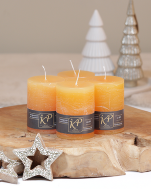Vier Tischkerzen in sonnengelb dekorativ auf einem Holztisch mit Weihnachtsdeko im Hintergrund.