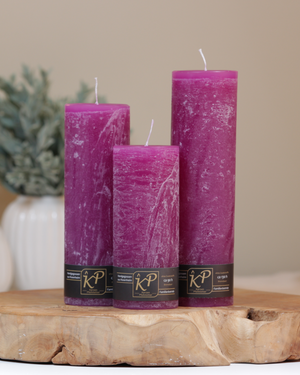 Blütenkerzen in magenta in drei Größen – dekorativ auf einem Holztisch mit Pflanze im Hintergrund.
