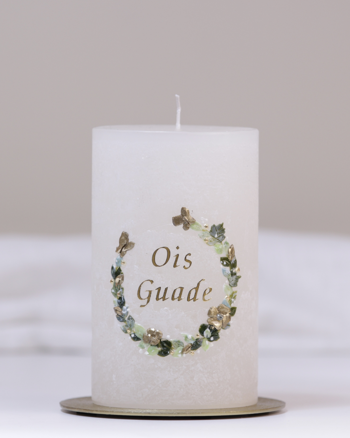 Geburtstagskerze in Elfenbein mit grün-goldenem Blumenkranz und dem Schriftzug ‚Ois Guade‘ – handgegossen und verziert.