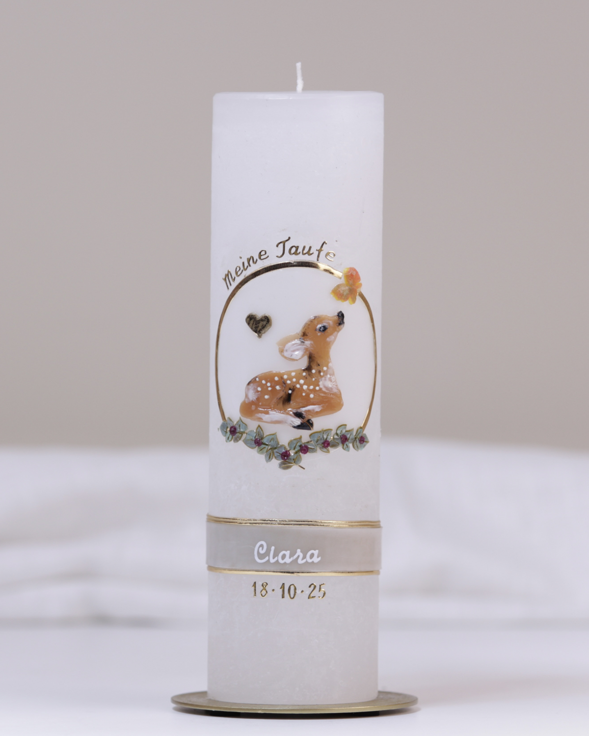 Weiße Taufkerze mit lila-goldener Verzierung aus handgeformtem Rehkitz, Blumenranke, Kreuz und Schmetterling.