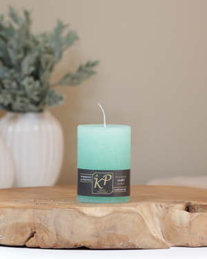 Tischkerze in mintgrün dekorativ auf einem Holztisch mit Pflanze im Hintergrund.